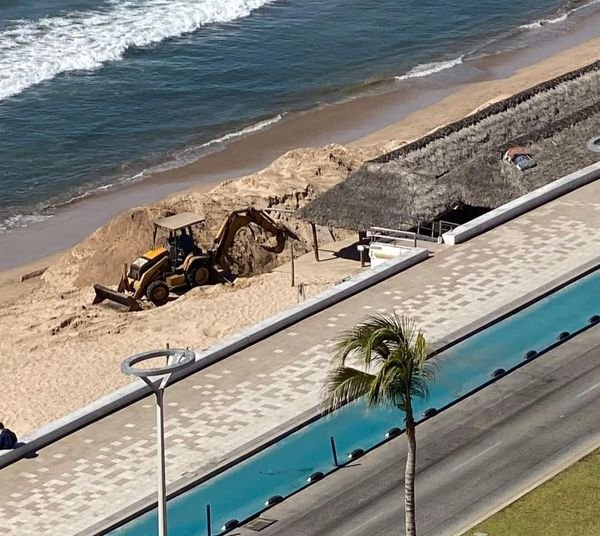 Una máquina excava en la playa, frente al malecón de Mazatlán, a un lado de un á